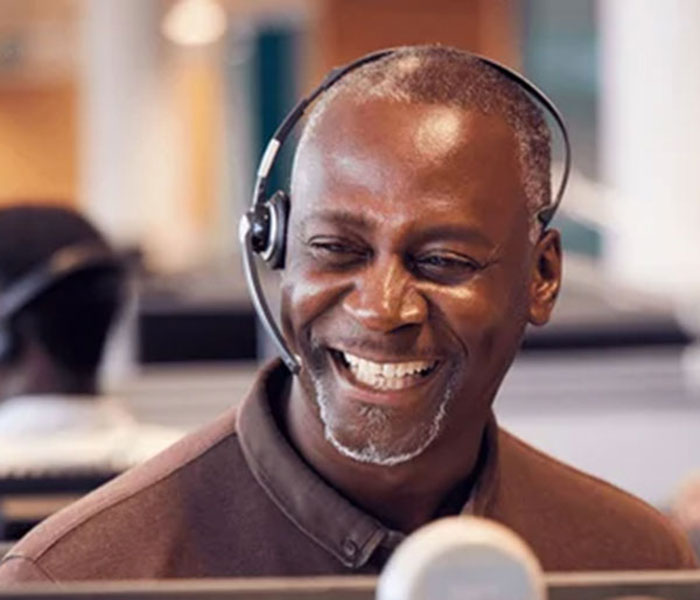 Smiling man wearing a headset sits in front of a computer