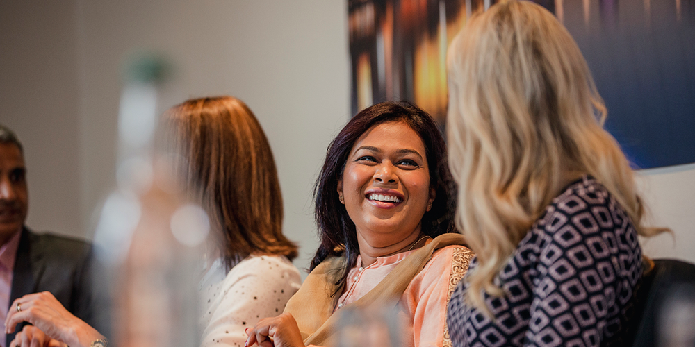 Two women talking and laughing together at a conference table.