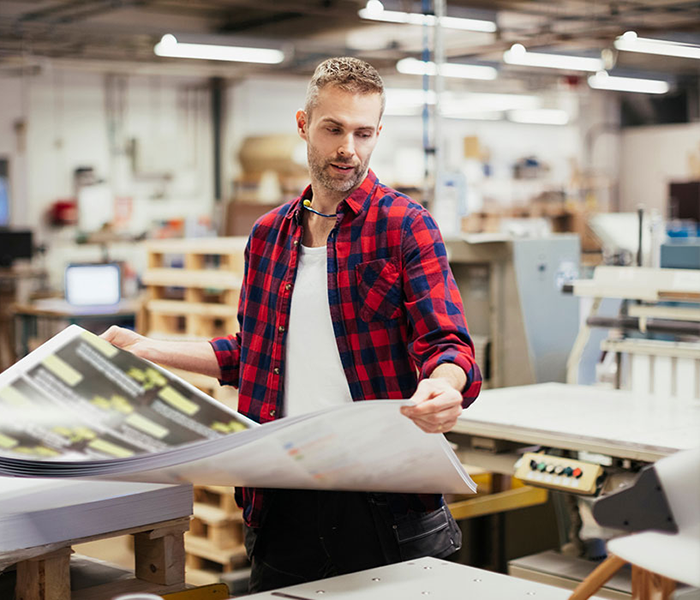 Man in a print manufacturing facility looking at a pile of printed material